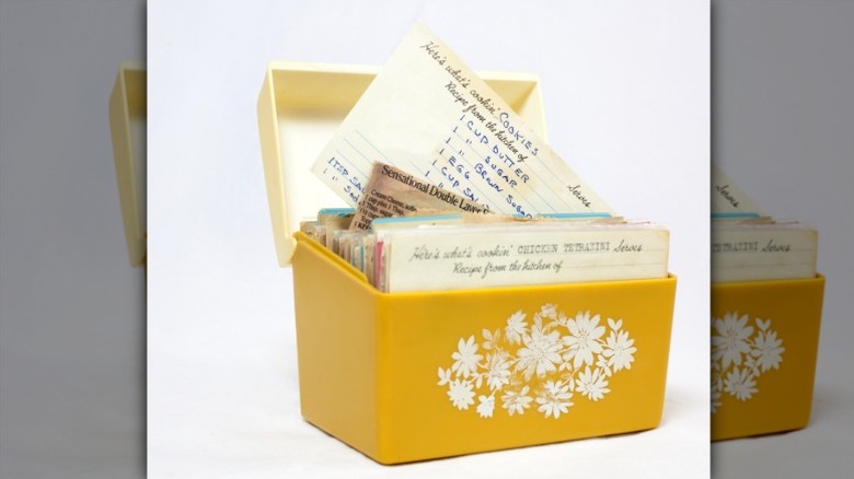 1960s yellow recipe box with a white floral design filled with hand-written recipe cards