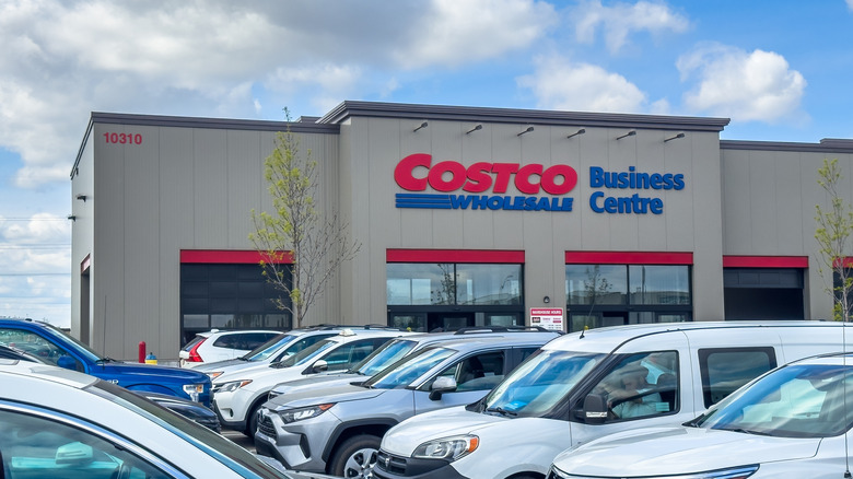 A Costco Business Center parking lot with several parked cars in the foreground and a Costco store front behind them.