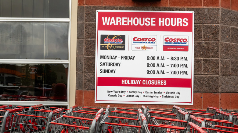 A board with Costco branding displaying operating hours outside a store.