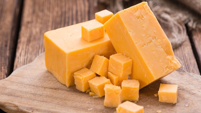Blocks and cubes of cheddar cheese on a wooden block