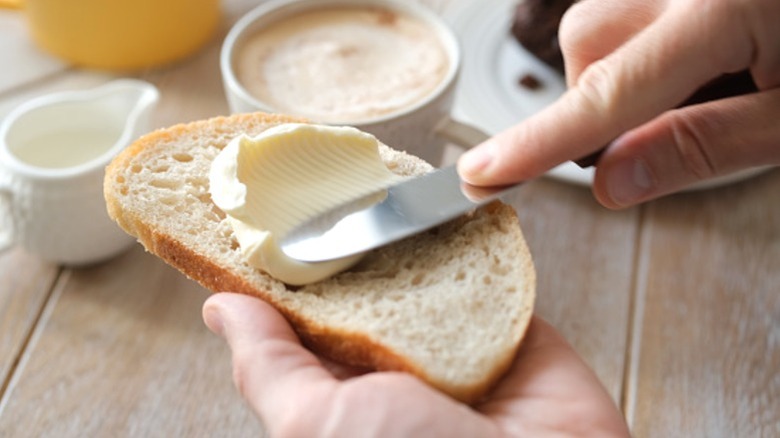 A person spreading butter on a piece of bread with a butter knife.