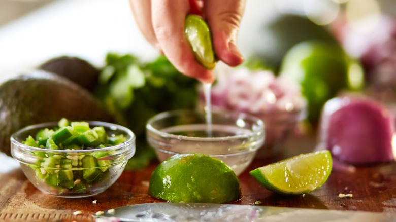 Person squeezing lime juice into glass bowl with various other ingredients around