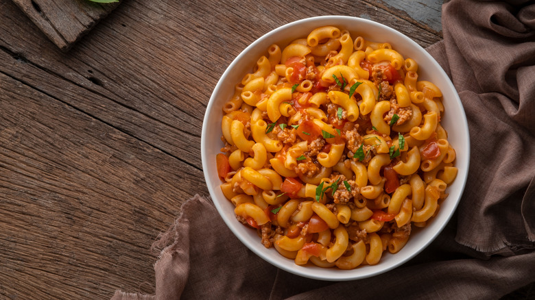 bowl of macaroni and cheese with ground meat and tomatoes on wooden table