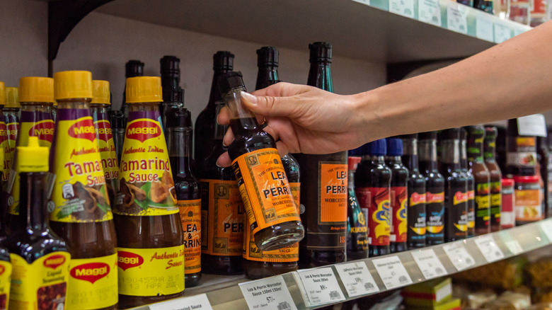 Person choosing a bottle of Lea & Perrins Worcestershire sauce from store shelf