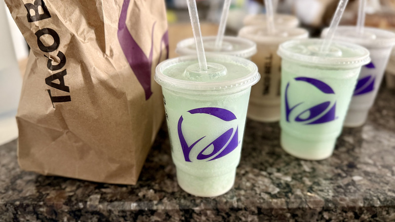 Collection of Taco Bell's Dirty Frozen Mountain Dew Baja Blasts in takeout cups on counter next to Taco Bell takeout bag