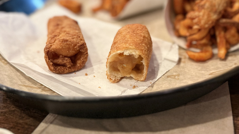 Bite taken out of one of Arby's Peach Cobbler Roll on plate next to curly fries