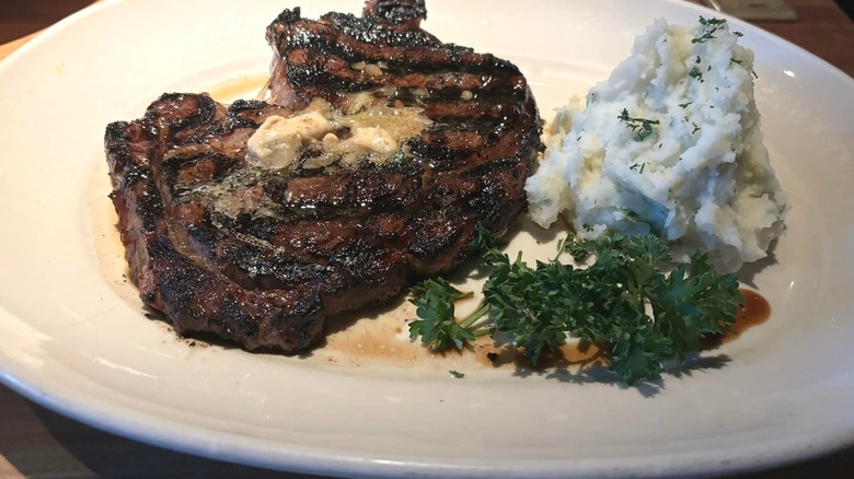 A butter-covered ribeye steak and mashed potatoes on a plate at Houston's chain restaurant.