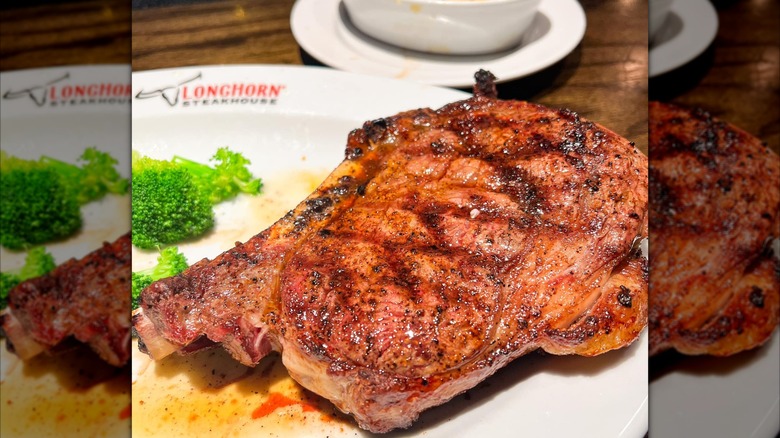 A large, bone-in ribeye steak and broccoli on a plate labeled longhorn at Longhorn Steakhouse chain restaurant.