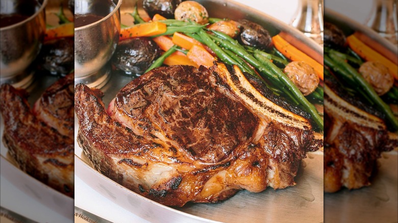 A juicy ribeye and cooked vegetables on silver tray at Smith & Wollensky chain restaurant.