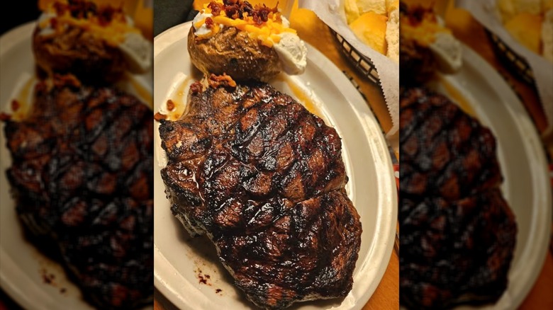 A cheesy baked potato and large ribeye steak on a white plate at Texas Roadhouse.
