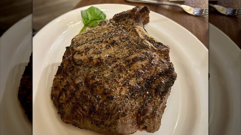 A large, glistening bone-in ribeye steak on a white plate at The Capital Grille chain restaurant.