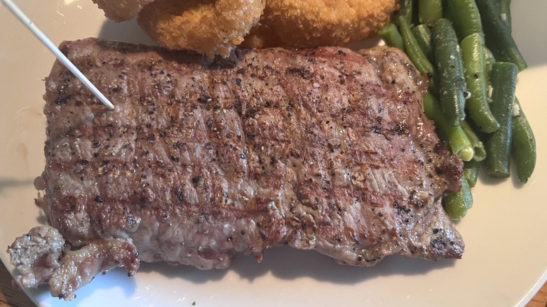 A rectangular piece on ribeye steak on a plate with onion rings and green beans at Applebee's chain restaurant.