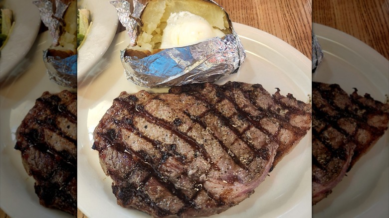 A large ribeye steak and a foil-wrapped baked potato on a white plate at Logan's Roadhouse chain restaurant
