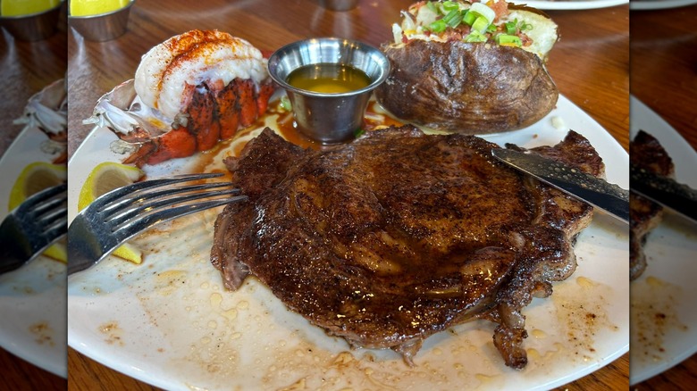 A surf-and-turf plate holding lobster, ribeye steak, and a baked potato and Outback Steakhouse.