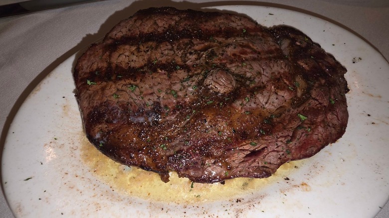 A large ribeye steak on a juice-splattered white plate at Ruth's Chris Steak House