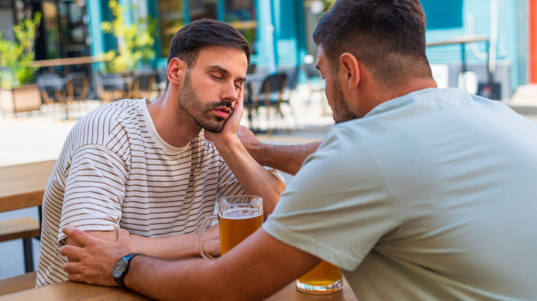 A man falling asleep while drinking beer while his friend tries to wake him up