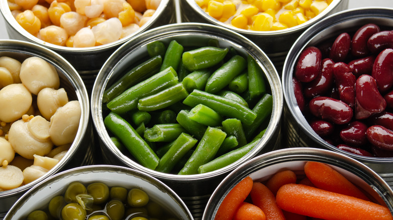 Canned vegetables in opened tin cans on kitchen table.