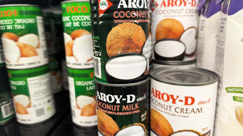 Various coconut milk and cream cans in grocery store aisle.