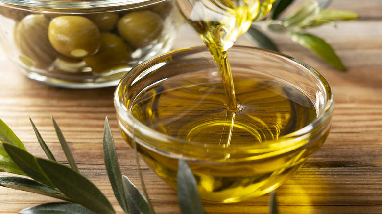 The moment olive oil is poured into a glass bowl set against a wooden background