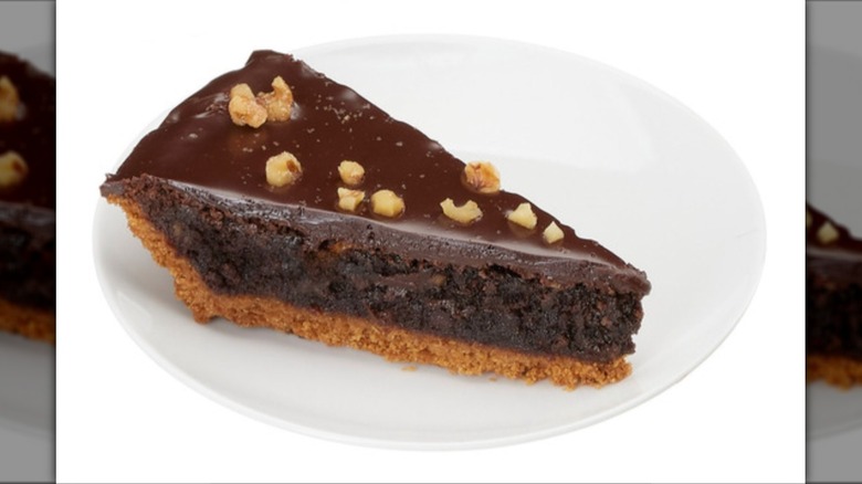 Slice of brownie walnut pie on white plate on a white background.