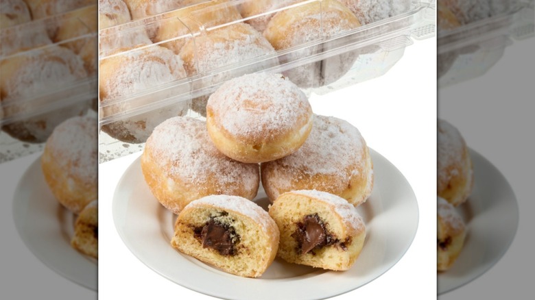 Four mini beignets filled with chocolate hazelnut on white plate with one sliced in half and filling showing with a package of mini beignets in the background.