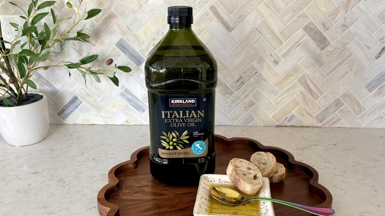 A 2-liter bottle of Kirkland Signature Italian extra virgin olive oil on a tray with sliced bread and dipping bowl of oil