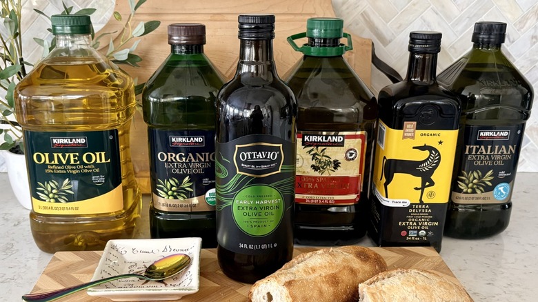 A lineup of jugs of Costco olive oils with French baguette, dipping bowl, and spoon