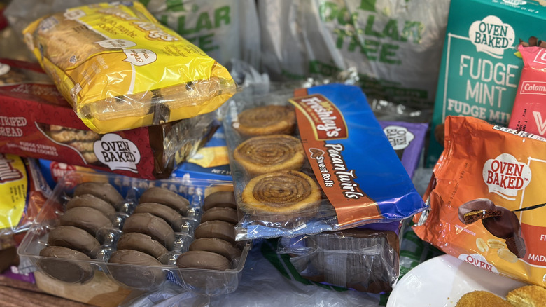 Dollar Tree deserts stacked on top of each other with plastic Dollar Tree shopping bags in the background, snacks include Oven Baked fudge mint cookies and Mrs. Freshley's Pecan Twists