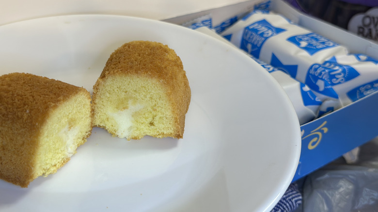 A Cravingz Spongiez Creme Filled Sponge Cake cut open, filling exposed, on a white plate next to package