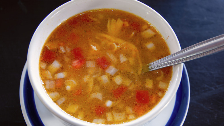 A white cup with broth-based soup and diced vegetables on saucer