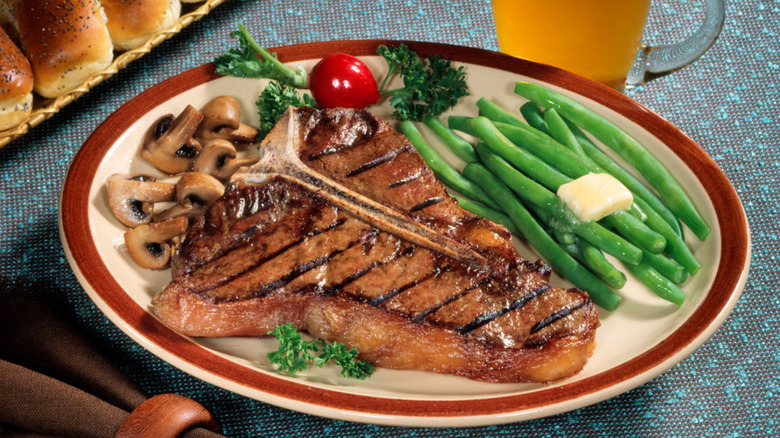 Grilled t-bone steak on a plate with a side of mushrooms and green beans with butter