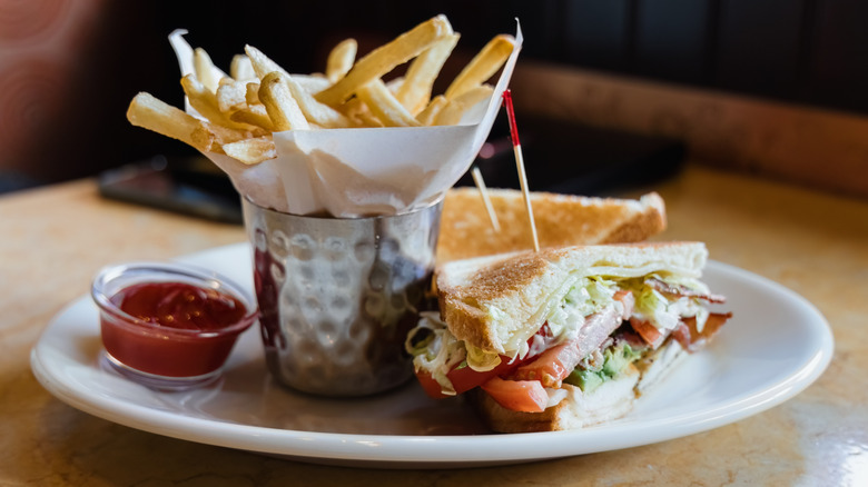 Close-up of grilled chicken and avocado club with side of fries on table at restaurant