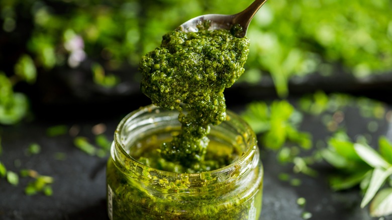 Spoon pulling pesto from glass jar