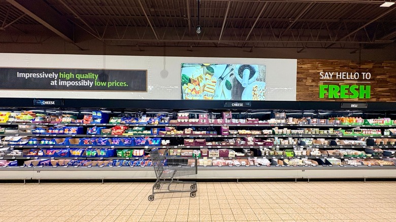 An empty shopping cart sitting in front of a refrigerated section at Aldi.