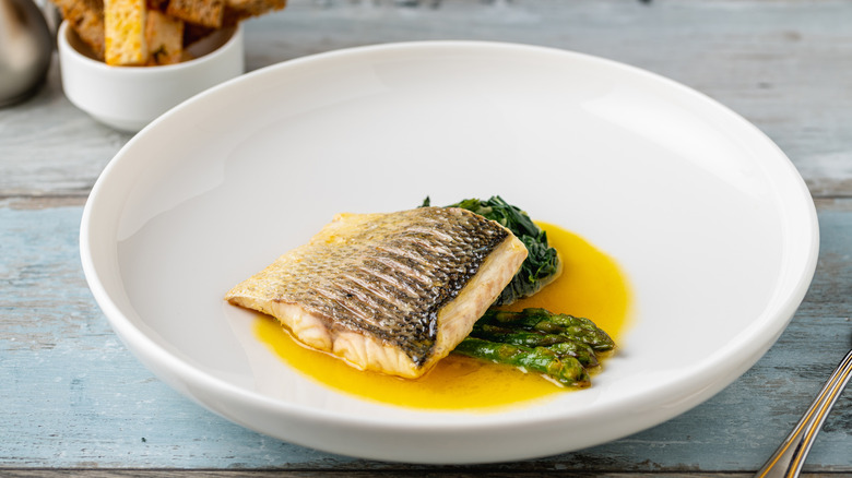 Piece of grilled sea bass in white dish with asparagus