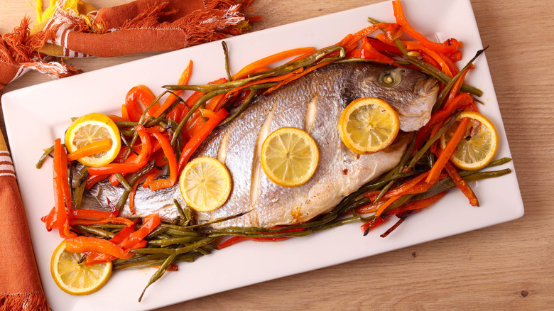 Baked mahi mahi on white tray with red peppers and lemons