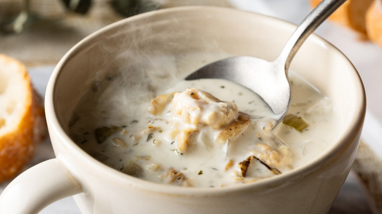 Spoon in white bowl of thick clam chowder