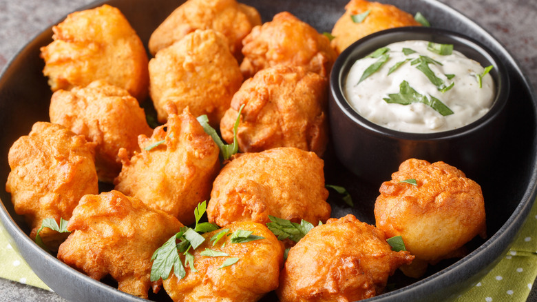 Hush puppies in black bowl with ramekin of tartar sauce