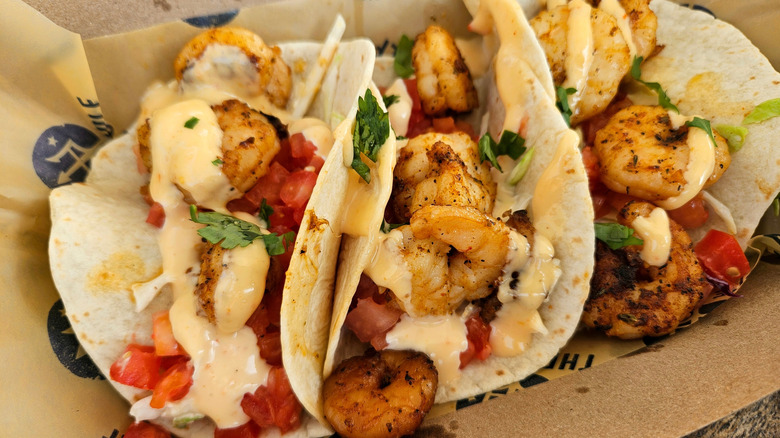 Three shrimp tacos with veggies and sauce in basket