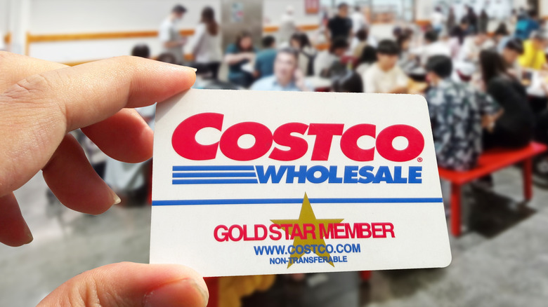 A person holding a Costco Wholesale membership card inside a Costco location