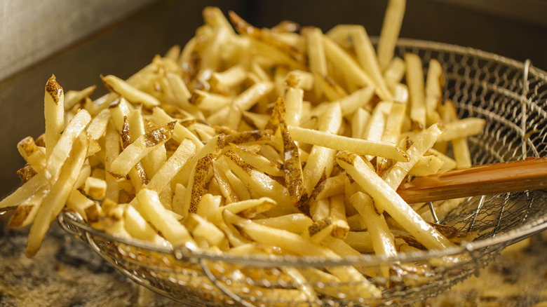 Scooping french fries out of frying oil using a metal basket strainer
