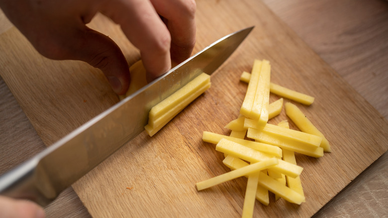 Using a chef's knife to cut potatoes into strips for french fries