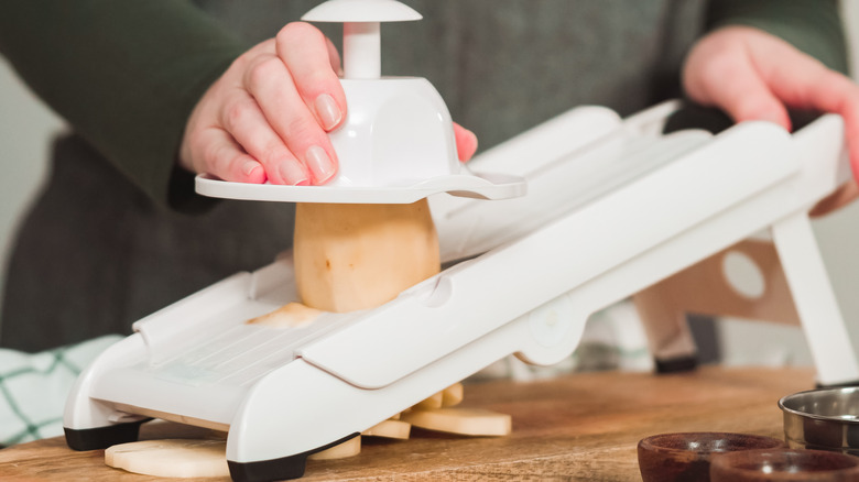 A woman slices a potato into discs using a mandoline cutter