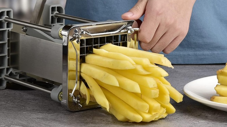 A cook presses a potato into strips using a metal fry cutter