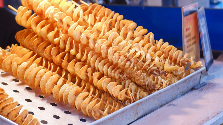 Spiral shaped fried potatoes on sticks in a metal street vendor bin