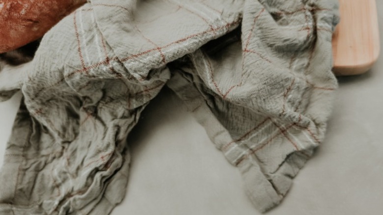a light green or gray baking towel next to a loaf of bread and wooden cutting board
