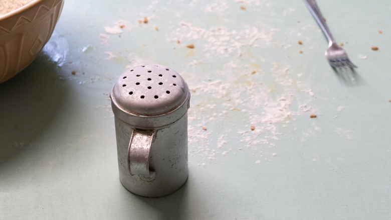 Metallic flour shaker on counter dusted with flour