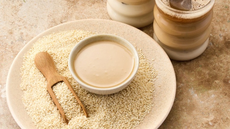 A small bowl of tahini surrounded with sesame seeds.