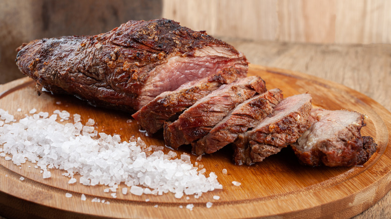 Sliced grilled beef on cutting board with pile of coarse salt