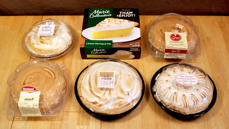 Six lemon meringue pies purchased from grocery stores in their packaging and arranged on a wooden table